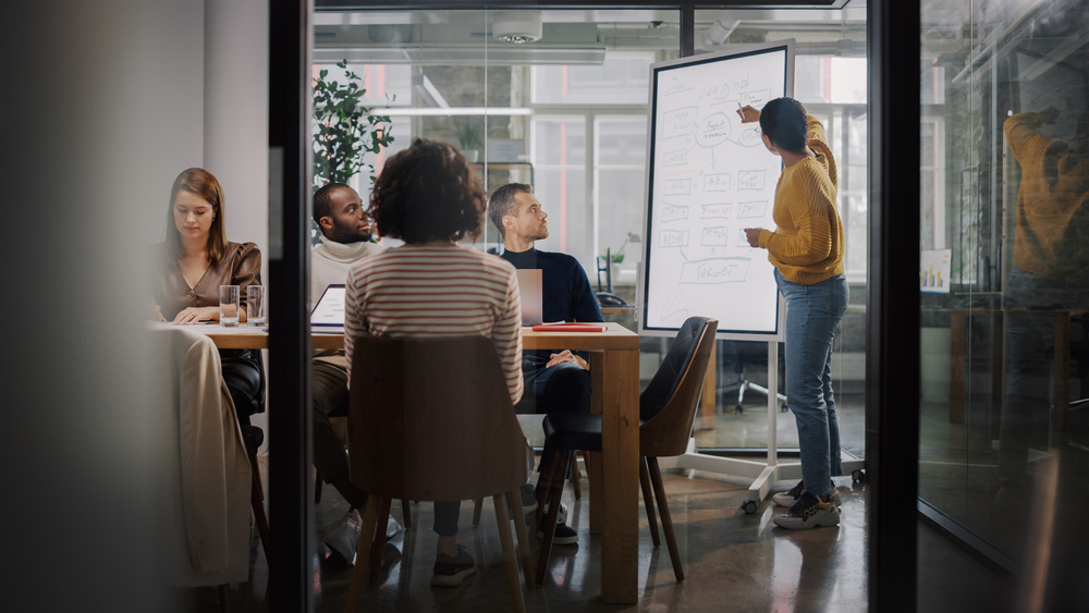 Digital Marketing Agency vs. In-House - Webtek Digital Marketing - A team sits in front of a woman presenting on a digital whiteboard